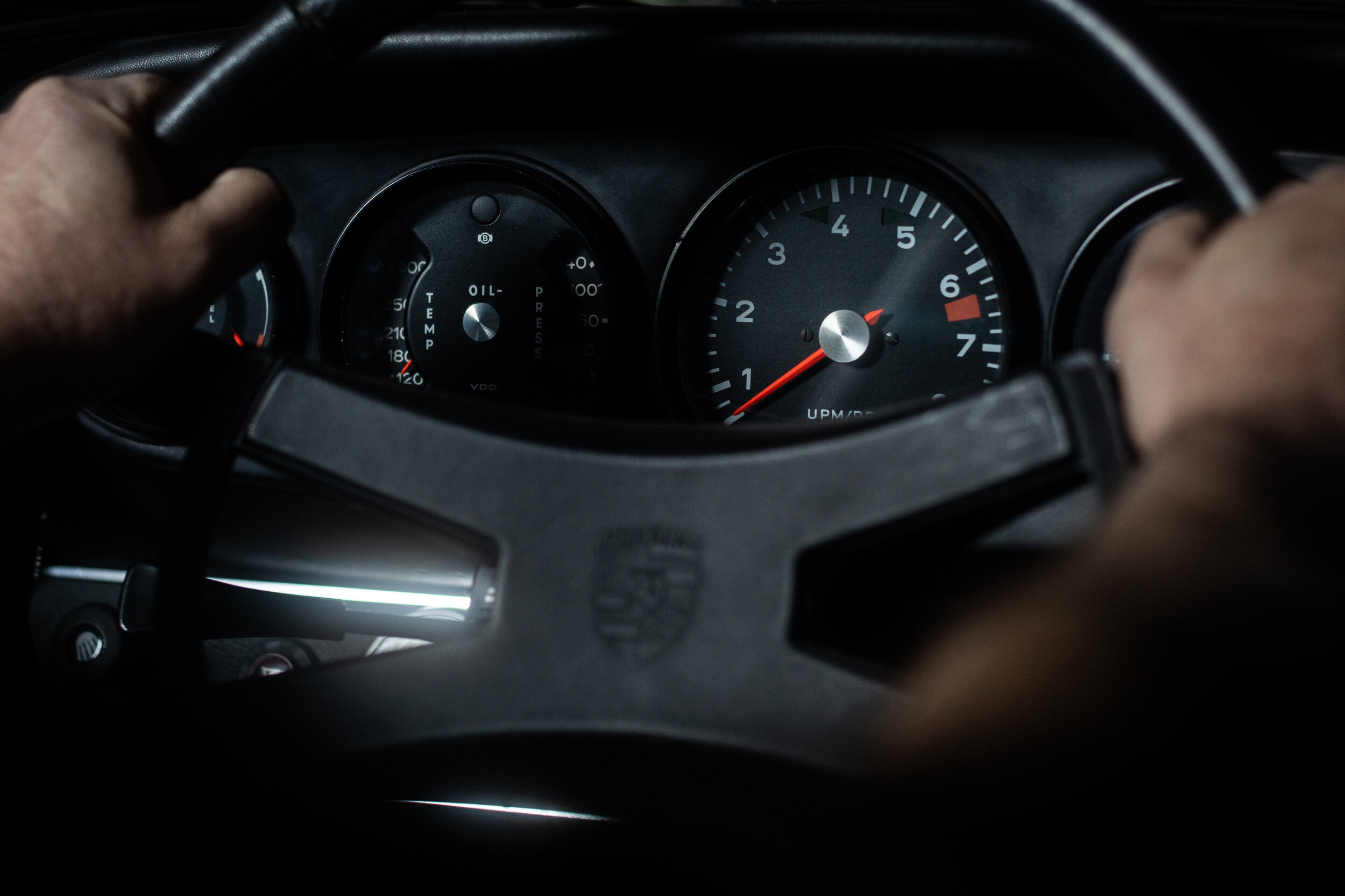 Hände am Lenkrad eines klassischen Porsche, dahinter die Rundinstrumente
