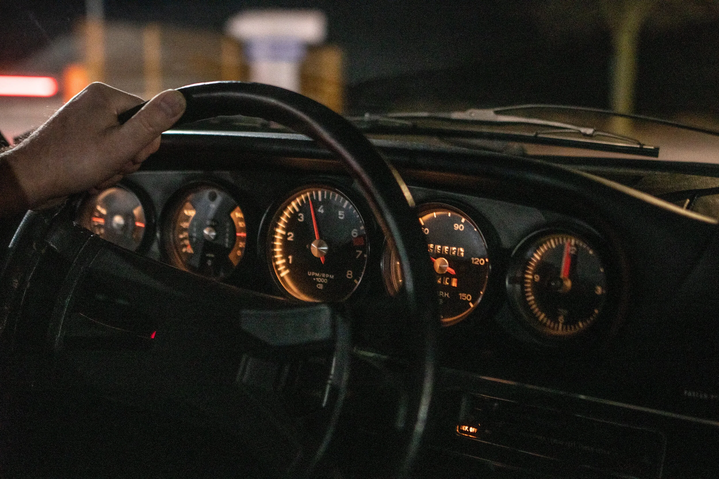 Hand am Lenkrad eines klassischen Porsche 911, die Instrumente leuchten orange
