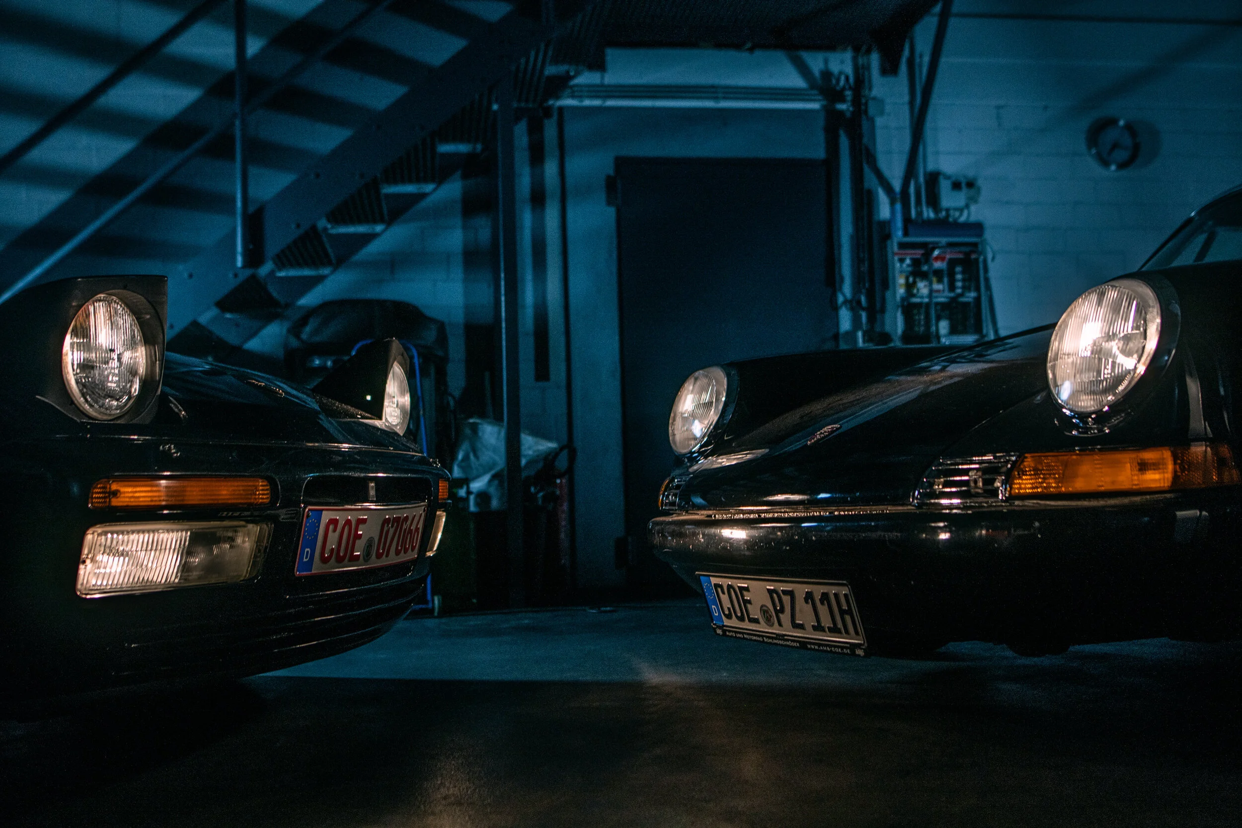 Zwei klassische Porsche 911 mit eingeschalteten Scheinwerfern in der AMS Werkstatt